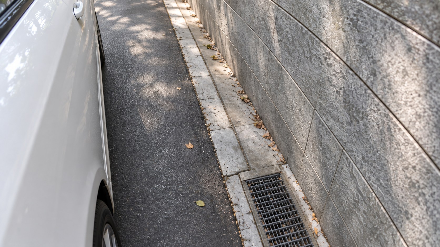 車外後視鏡下方視角，觀察白色車身與灰色石牆之間的空間